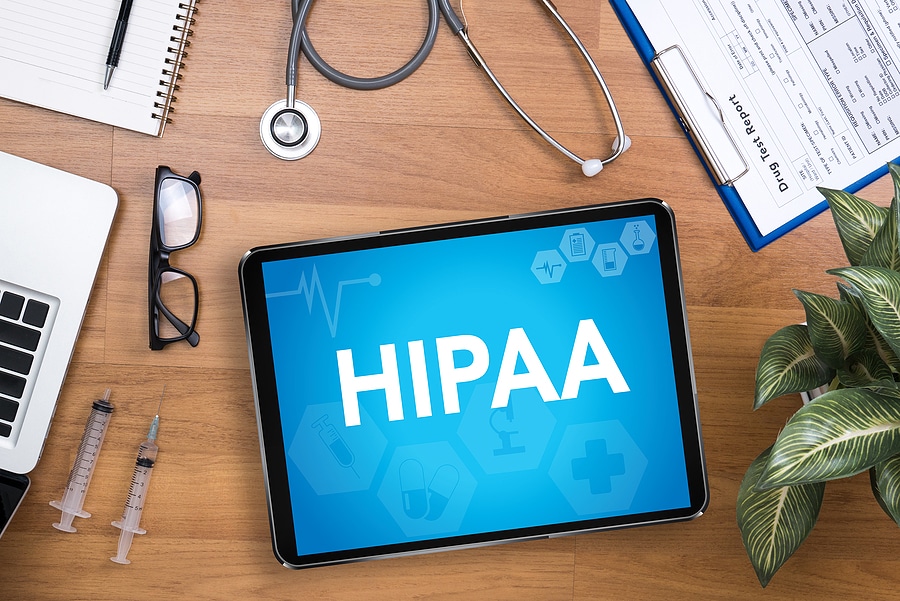 Top view of medical documents, a stethoscope, glasses, and a tablet with the word HIPAA
