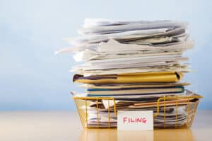 An old yellow wireframe filing tray piled high with documents and folders