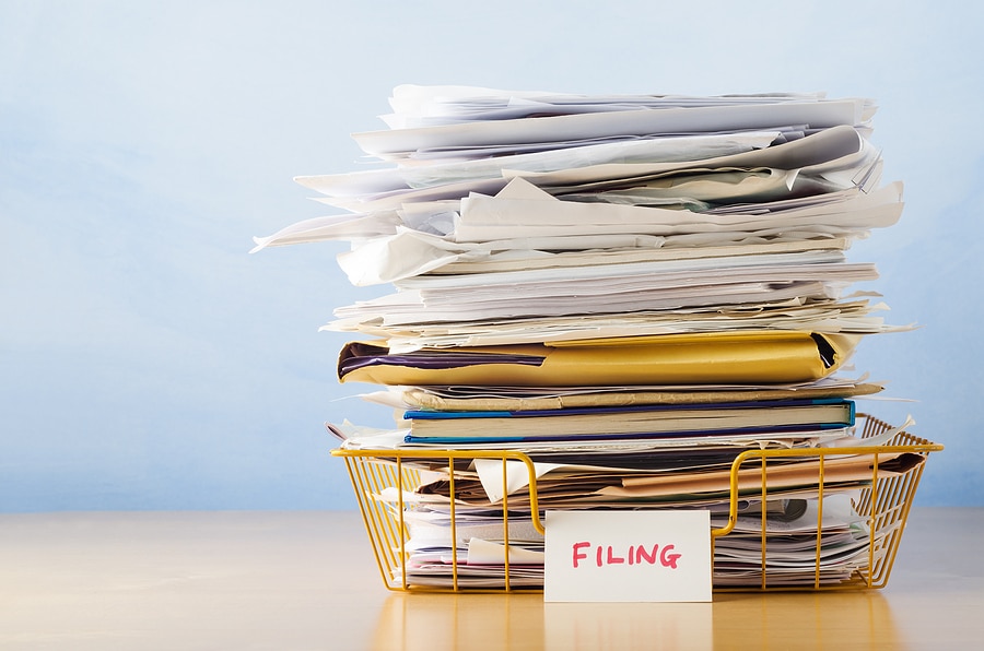 An old yellow wireframe filing tray piled high with documents and folders