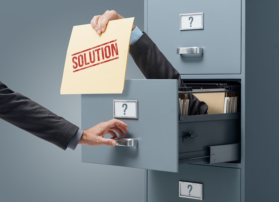 Businessman inside a filing cabinet giving a file with business solutions to an office clerk